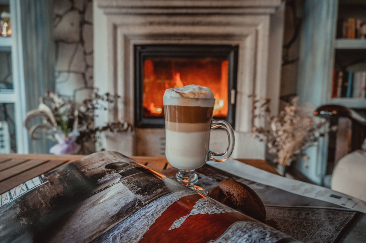 A frothy cappuccino on a table beside a cozy fireplace, creating a warm and relaxing ambiance.